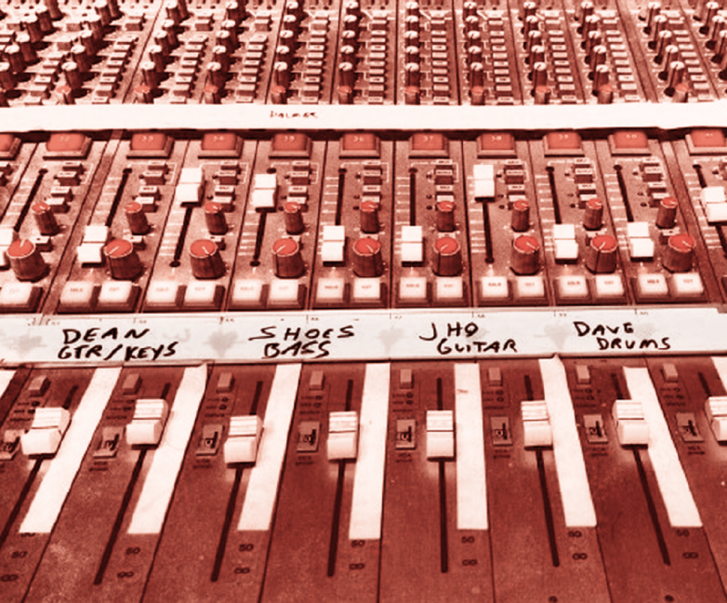 Exemple d’une table de mixage ( détail du bas ) avec ses tranches, potentiomètres et surtout, sa bande de rouleau adhésif sur laquelle sont inscrits les noms des musiciens auxquels se rattachent les pistes sonores et leurs paramètres respectifs.